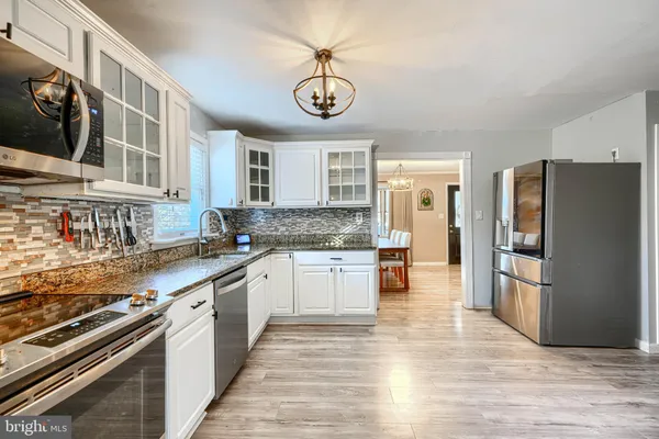 a kitchen with stainless steel appliances granite countertop a refrigerator a sink dishwasher a stove and white countertops with wooden floor