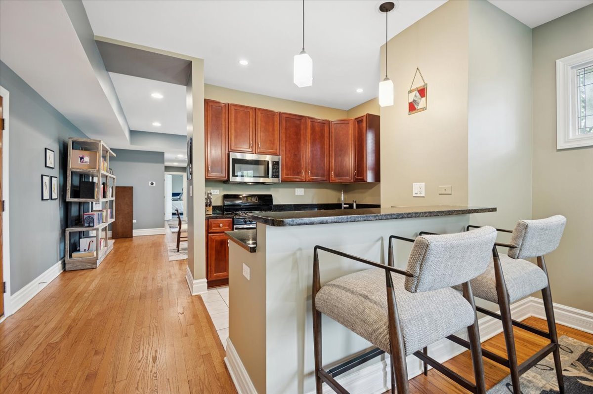 1265 West Granville Avenue, Unit 3 Chicago, IL 60660 - Photo 4 of 15 a kitchen with stainless steel appliances granite countertop a stove top oven a sink a dining table and chairs with wooden floor