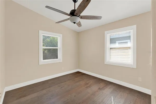 an empty room with wooden floor ceiling fan and windows