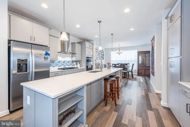 a kitchen with stainless steel appliances a refrigerator a sink dishwasher a oven and a dining table with wooden floor