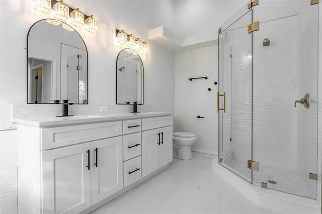 a bathroom with double vanity sinks a toilet a shower and a mirror