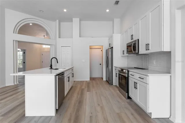 a kitchen with stainless steel appliances a stove a sink a refrigerator and white cabinets with wooden floor