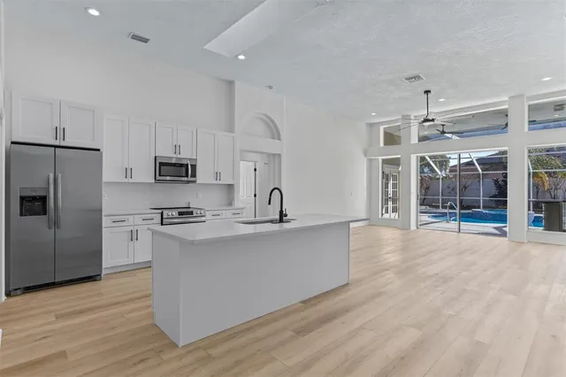 a large kitchen with stainless steel appliances a stove a sink dishwasher a refrigerator white cabinets and wooden floor