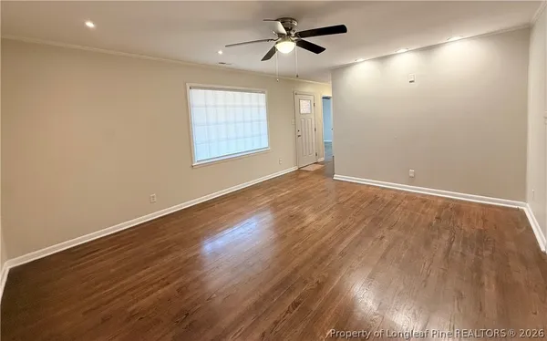 an empty room with wooden floor ceiling fan and windows
