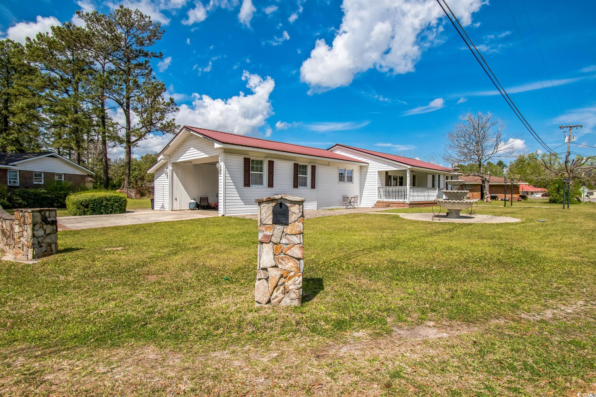 Rear view of house featuring concrete driveway, a carport, a yard, and a metal roof