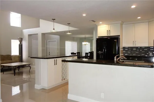 a kitchen with stainless steel appliances kitchen island granite countertop a refrigerator a sink a stove and white cabinets with wooden floor