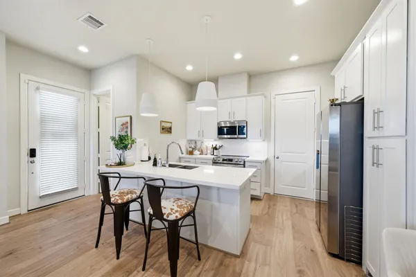 a kitchen with stainless steel appliances a dining table chairs refrigerator and cabinets