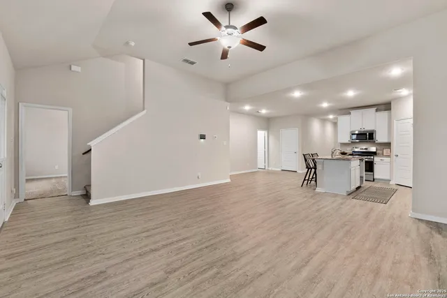 a view of an empty room with kitchen appliances and a ceiling fan