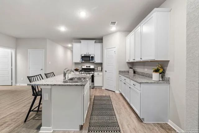 a kitchen with stainless steel appliances granite countertop a stove top oven a sink dishwasher and a refrigerator with wooden floor