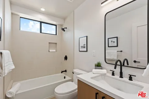 a bathroom with a granite countertop sink a toilet a mirror a bathtub and shower
