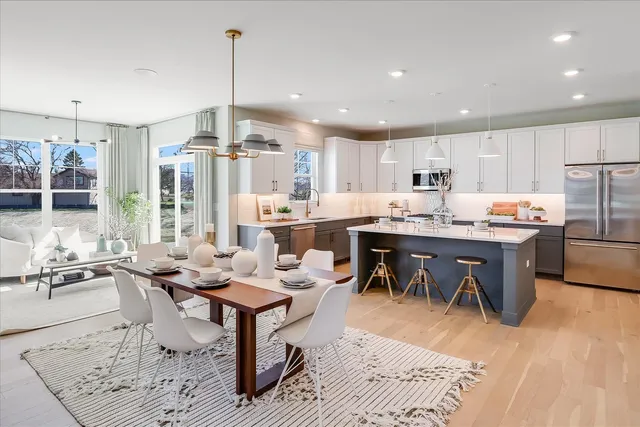 a open kitchen with stainless steel appliances granite countertop a stove a refrigerator a kitchen island a dining table and chairs with wooden floor