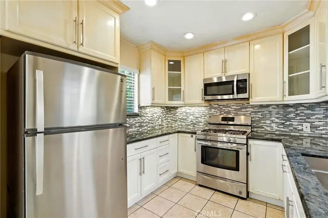 a white kitchen with stainless steel appliances granite countertop a refrigerator sink and microwave