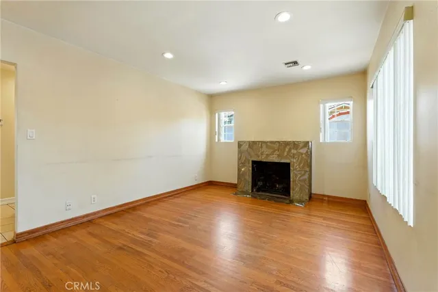 a view of an empty room with wooden floor fireplace and a window