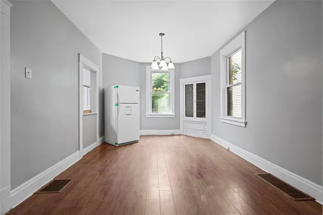 an empty room with wooden floor chandelier and windows