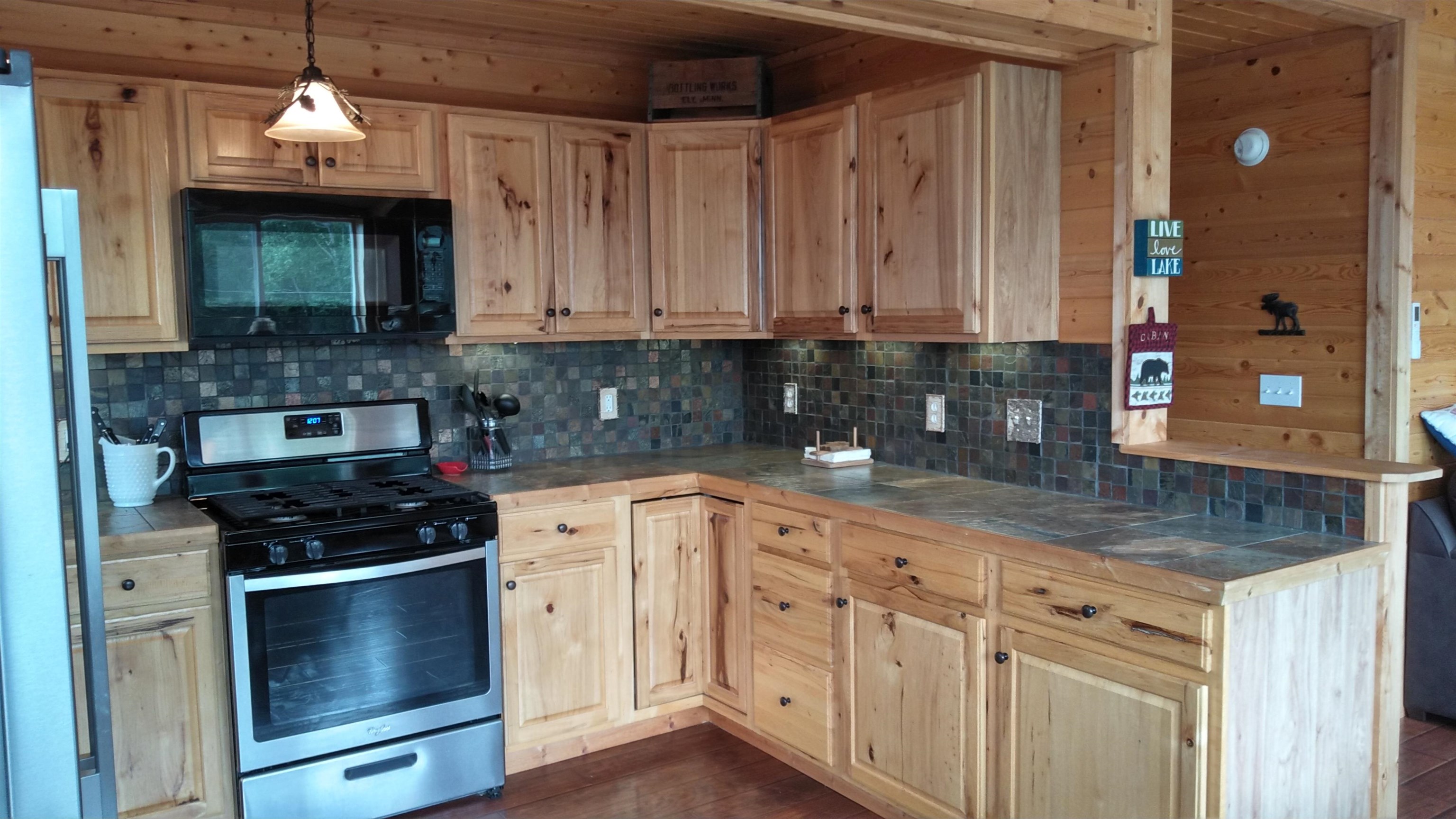 13496 Pine Road, Unit 10 Ely, MN 55731 - Photo 4 of 26 Kitchen featuring stainless steel range with gas cooktop, black microwave, tile counters, backsplash, and light brown cabinetry