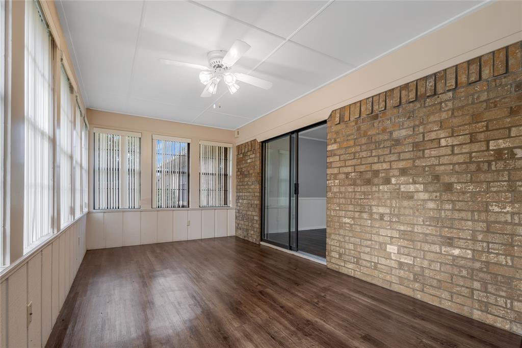 1609 Robin Street Mineola, TX 75773 - Photo 11 of 24 Enclosed sunroom featuring extensive window panels, wood-finish flooring, a ceiling fan with integrated lighting, a brick accent wall, and sliding glass doors