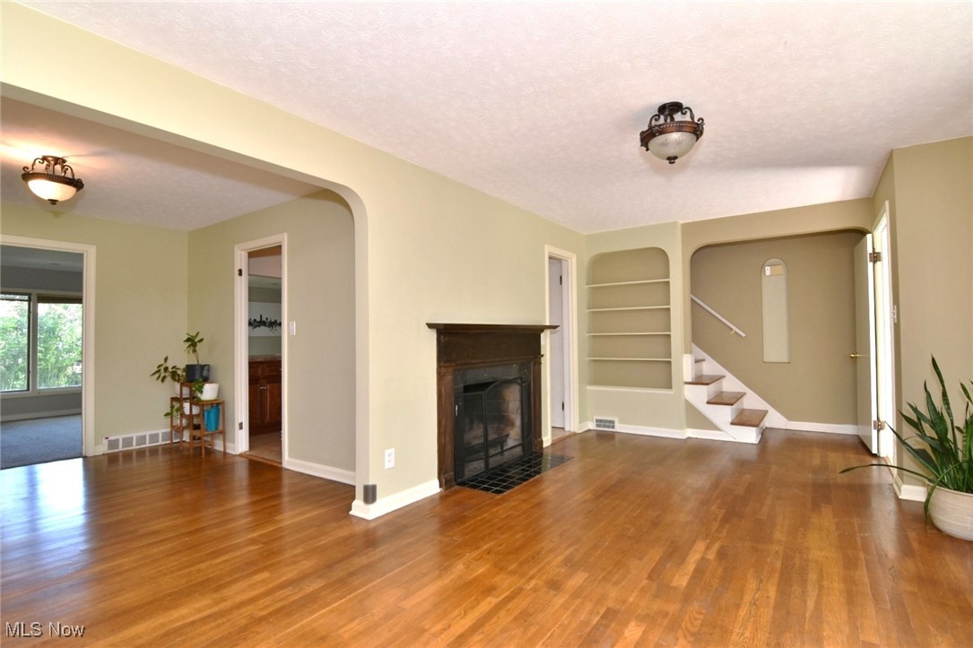 3679 Fenley Road Cleveland Heights, OH 44121 - Photo 9 of 45 Unfurnished living room featuring built in shelves, a textured ceiling, stairway, wood finished floors, and a fireplace with flush hearth
