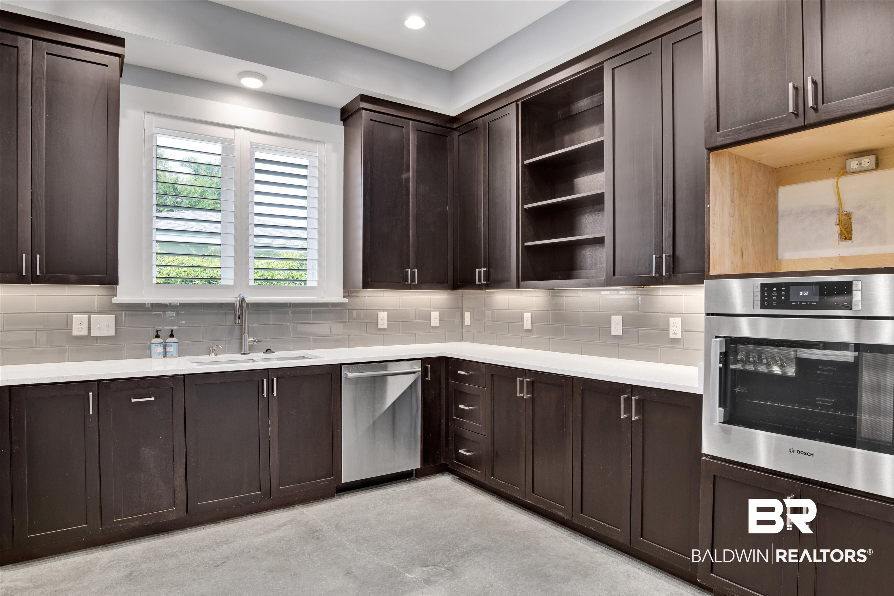 27980 Canal Road Orange Beach, AL 36561 - Photo 23 of 46 Kitchen featuring open shelves, decorative backsplash, light countertops, dark brown cabinetry, and stainless steel appliances
