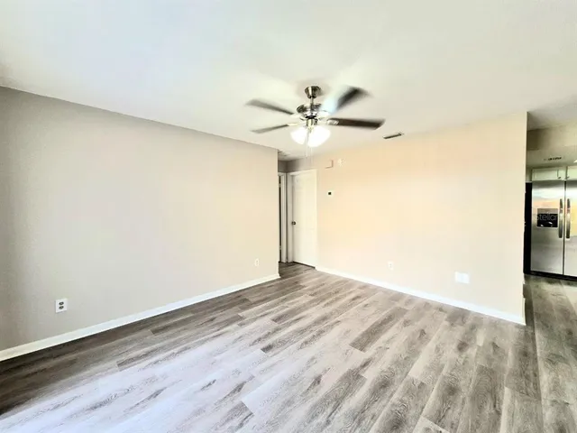 an empty room with wooden floor fan and windows