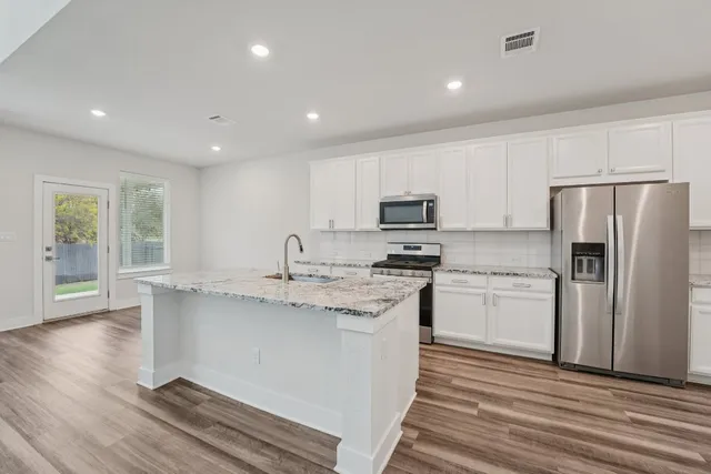 a kitchen with stainless steel appliances granite countertop a refrigerator a sink dishwasher a stove and white countertops with wooden floor