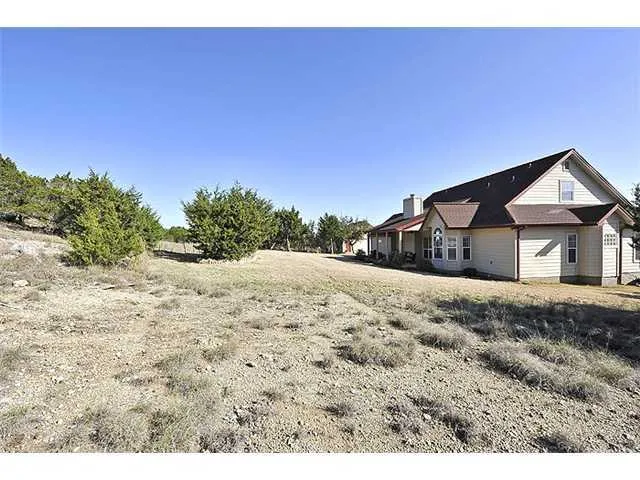 a view of a dry yard with trees in the background