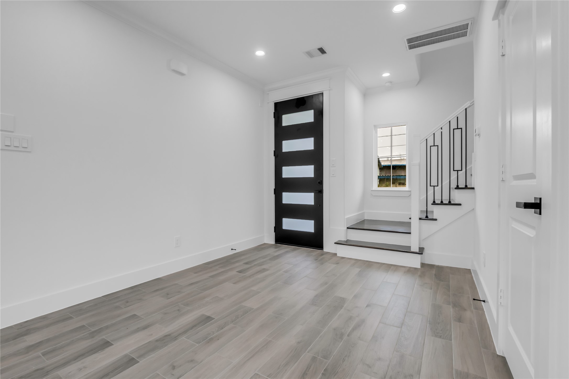 3168 Golfcrest Houston, TX 77087 - Photo 12 of 30 This modern entryway features sleek wood flooring, a striking black front door with frosted glass panels, and a staircase with contemporary railings. The space is bright and welcoming, offering a clean, minimalist aesthetic.