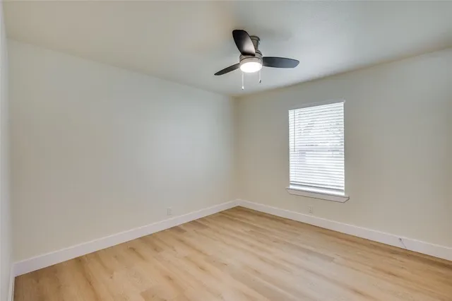 an empty room with wooden floor chandelier fan and windows