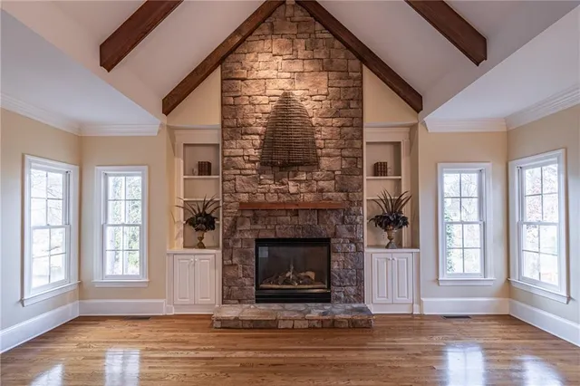 an empty room with wooden floor fireplace and windows