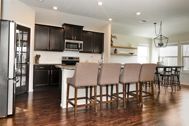 a kitchen with stainless steel appliances granite countertop a dining table chairs refrigerator and microwave