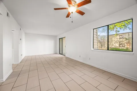 a view of an empty room with window and chandelier fan