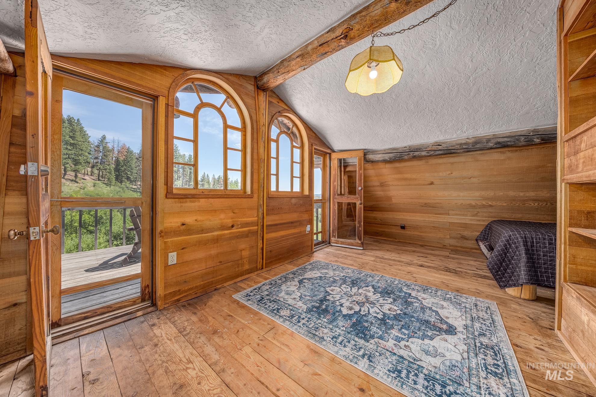 2150 Seid Creek Road Cambridge, ID 83610 - Photo 19 of 50 Wood-paneled interior featuring arched windows, wood-finish flooring, exposed ceiling beams, and a built-in shelving unit