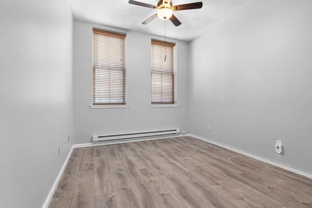 an empty room with wooden floor fan and windows
