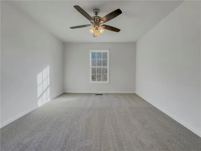 an empty room with ceiling fan and windows