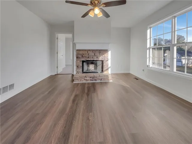 a view of an empty room with wooden floor fireplace and a window
