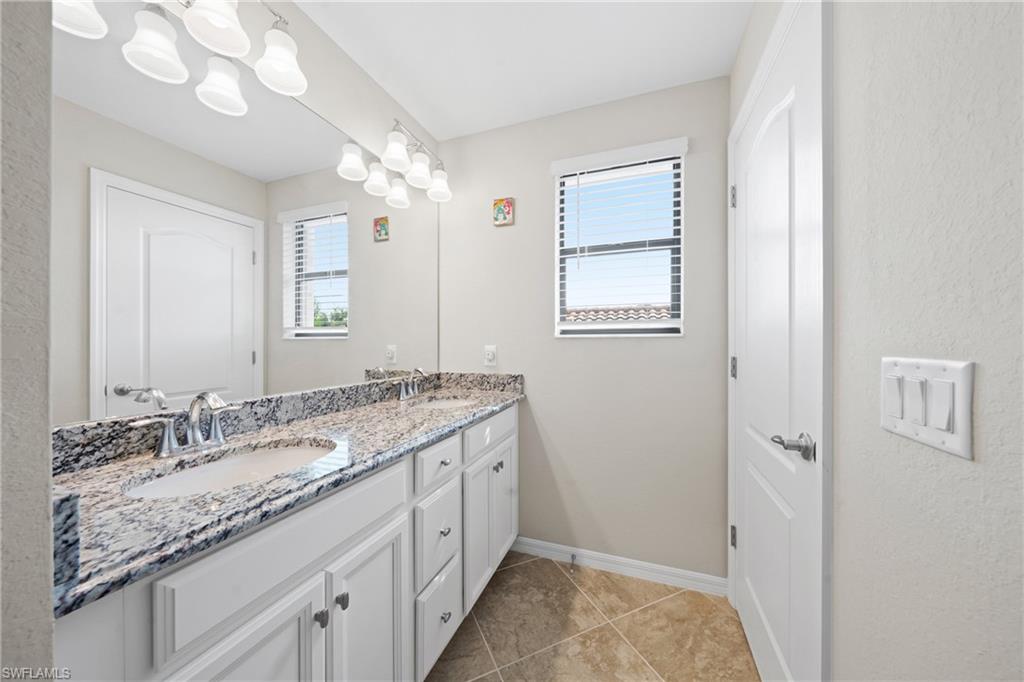4228 Raffia Palm Circle Naples, FL 34119 - Photo 26 of 50 Bathroom with double vanity, light tile patterned floors, and a textured wall