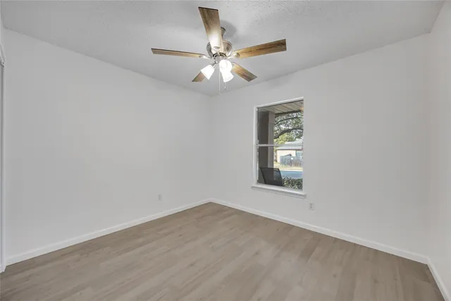 an empty room with wooden floor chandelier fan and windows