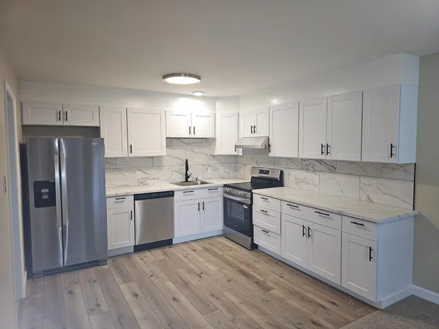 a kitchen with a sink dishwasher a refrigerator and white cabinets with wooden floor