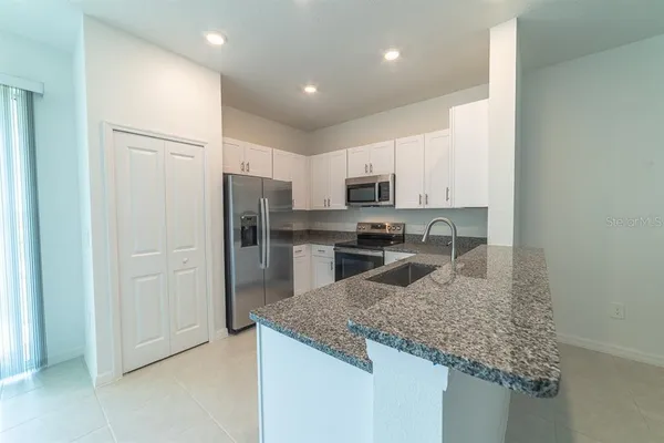 a kitchen with kitchen island granite countertop a sink a refrigerator and white cabinets