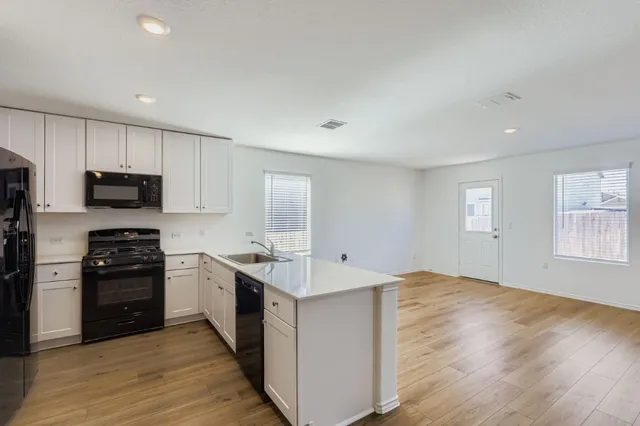 a kitchen with stainless steel appliances granite countertop a stove top oven a sink dishwasher and a refrigerator with wooden floor