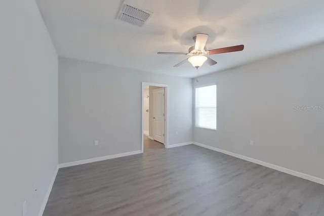 an empty room with wooden floor ceiling fan and window