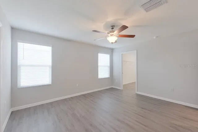an empty room with wooden floor and window with a ceiling fan