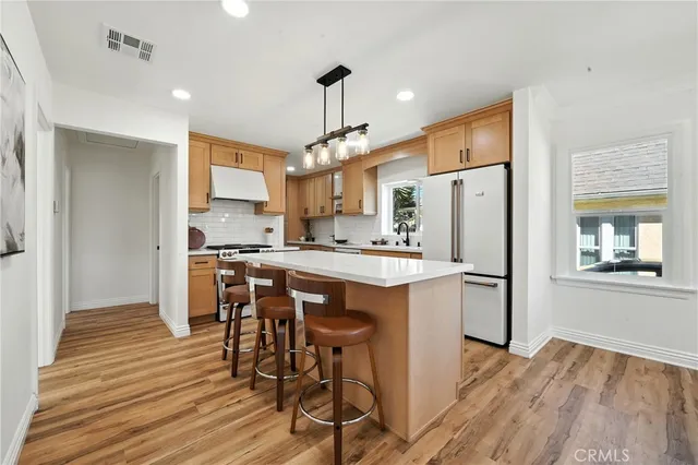 a kitchen with stainless steel appliances kitchen island granite countertop a refrigerator a stove a sink dishwasher and white cabinets with wooden floor