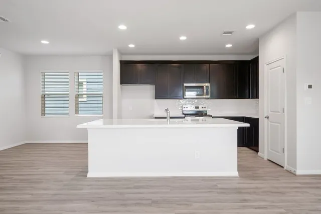 a living room with stainless steel appliances kitchen island granite countertop a stove a sink a refrigerator and white cabinets with wooden floor