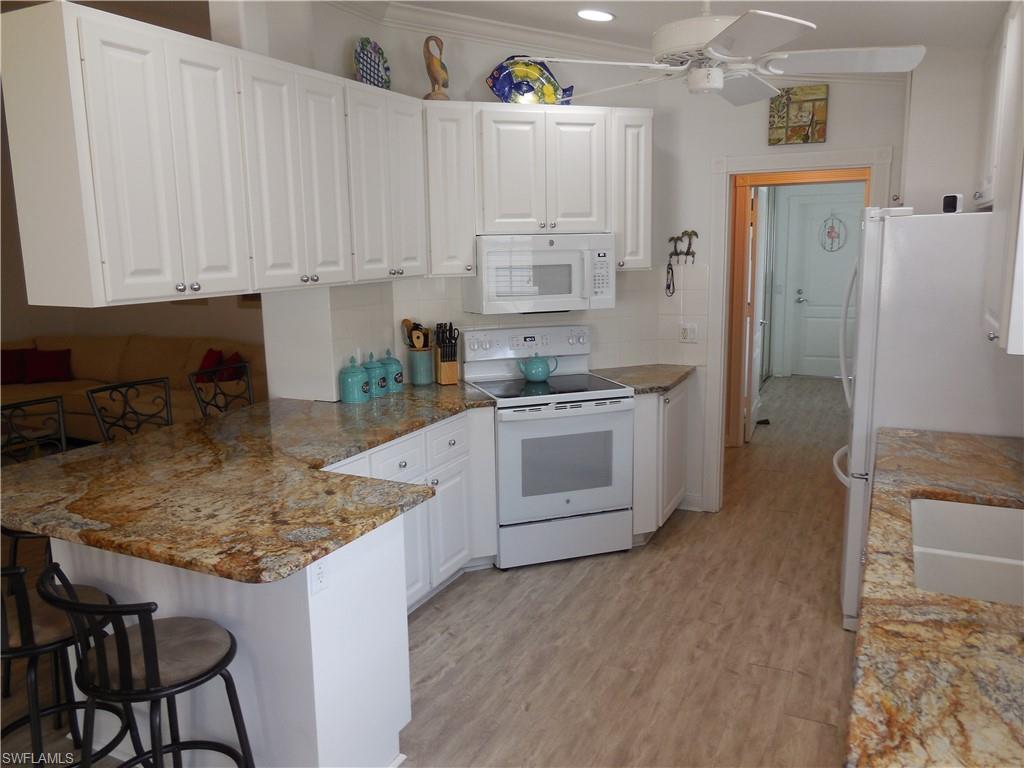4663 Ossabaw Way Naples, FL 34119 - Photo 4 of 44 Kitchen with a peninsula, white cabinets, white appliances, and a kitchen breakfast bar