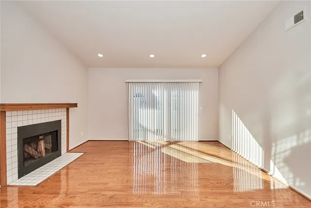 a view of an empty room with wooden floor fireplace and a window