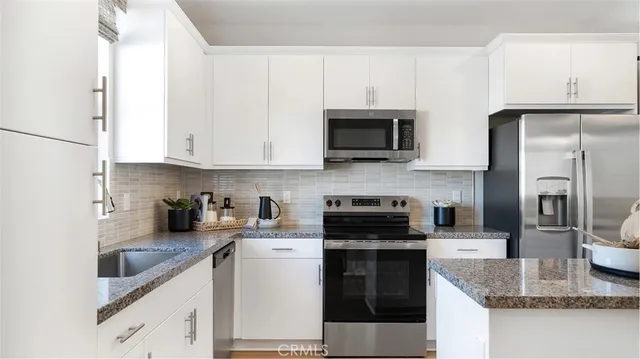 a kitchen with stainless steel appliances granite countertop a refrigerator a stove a sink and white cabinets