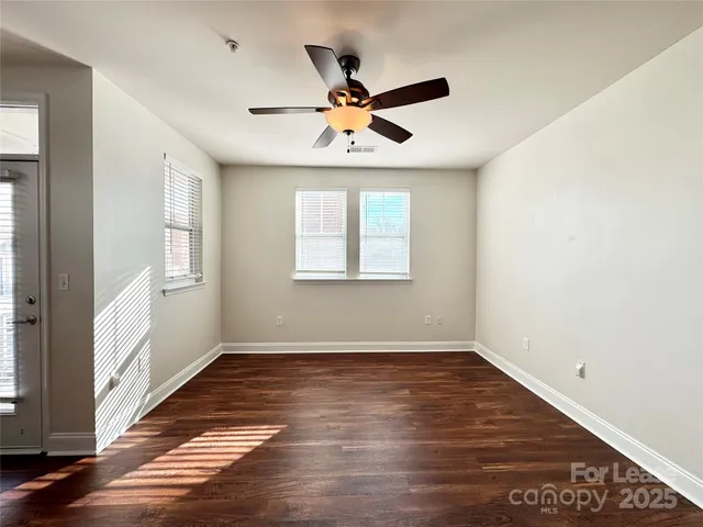 an empty room with wooden floor a ceiling fan and windows