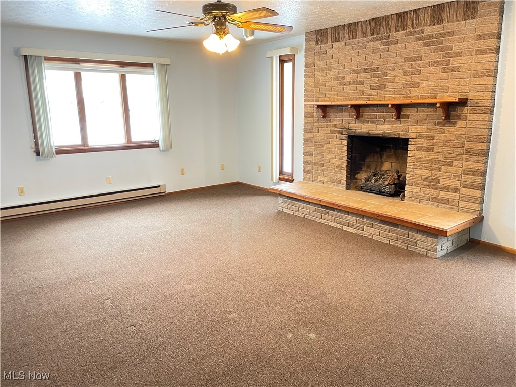 1381 Robb Road Conneaut, OH 44030 - Photo 18 of 50 Unfurnished living room featuring carpet floors, a baseboard radiator, a fireplace, a textured ceiling, and a ceiling fan