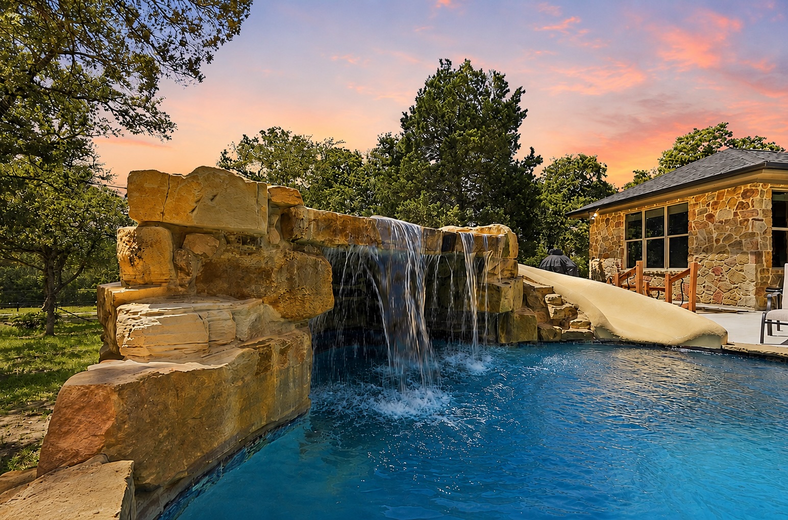 387 Corral Road Smithville, TX 78957 - Photo 2 of 40 Custom-designed swimming pool with a rock waterfall feature, integrated water slide, and stone-clad pool house