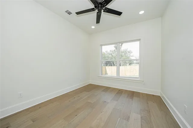 an empty room with wooden floor fan and windows